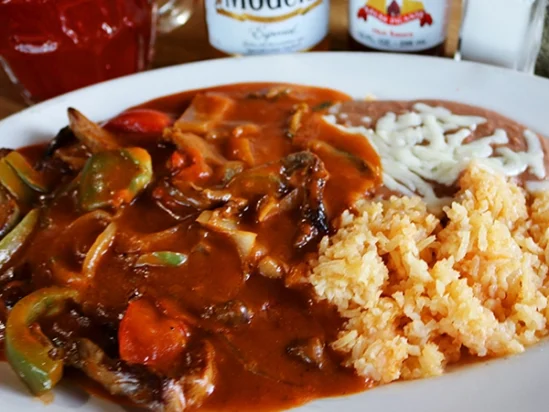 Beef with a spicy red sauce served with rice and beans